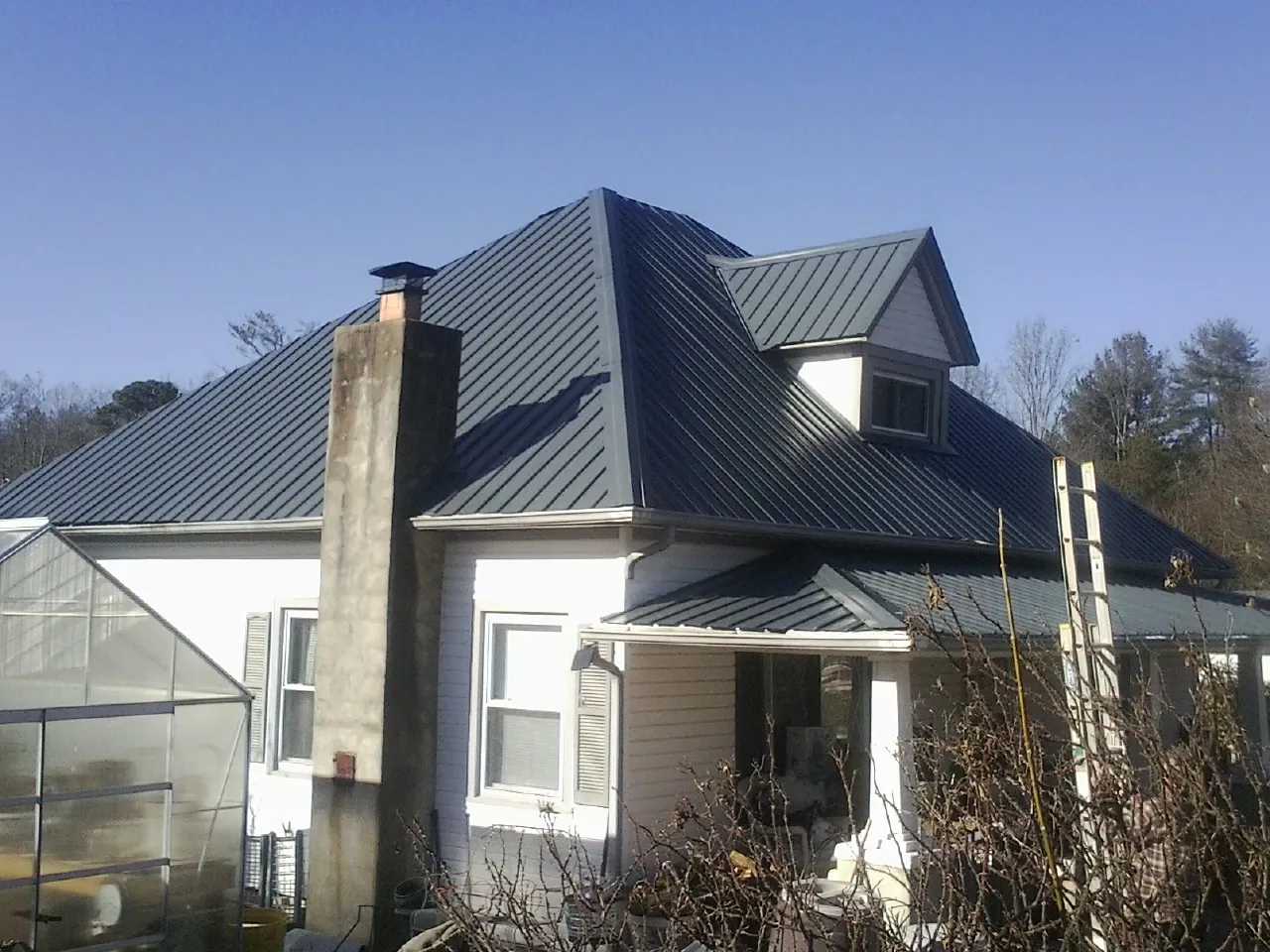 Dark blue standing seam metal roof on a white farmhouse with dormer — Slate & Tile Roof Repair by Roofing Brothers in Charlo
