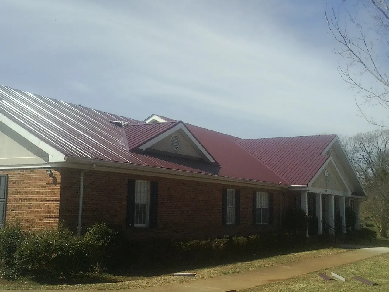 Red metal roof with gabled entries on a long brick building, from a Hail Damage Roof Repair job in Charlo