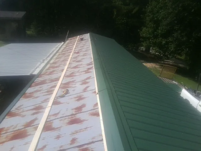 Old rusted panels beside newly installed green metal roofing — Wind Damage Roof Repair by Roofing Brothers in Charlo