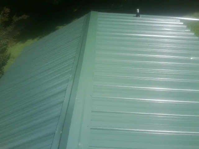 New green metal panels meeting at the ridge of a roof — Flat Roof Repair work by our crew in Charlo