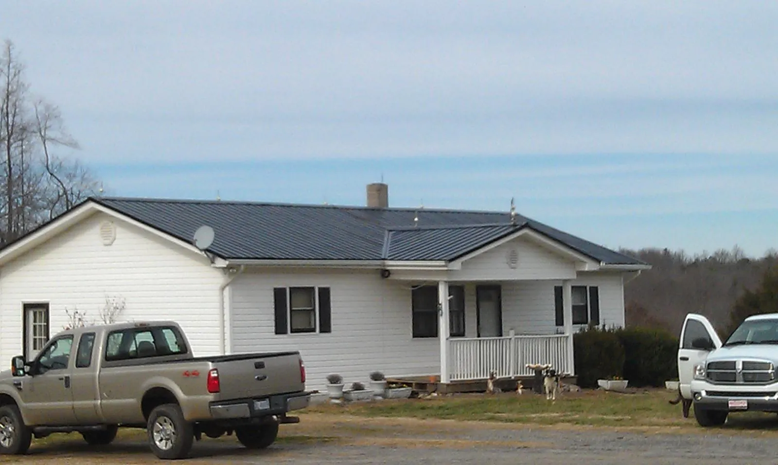 Finished dark metal roof on a white ranch home with work trucks parked in Charlo