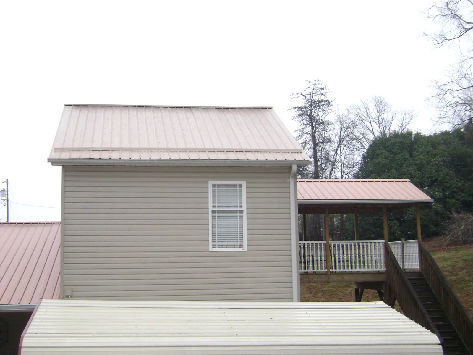 Tan metal roofs on a two story addition and attached porch, from a Roof Replacement job in Charlo